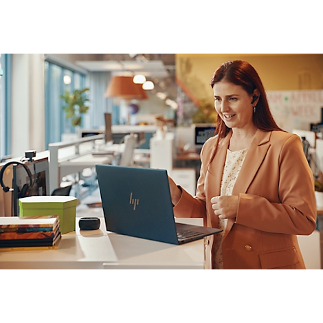 A woman in an office using a laptop. She is wearing a jacket and smiling while looking at the screen.