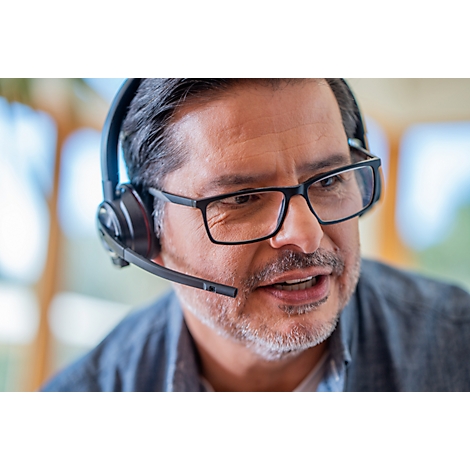A man wearing glasses and a headset is speaking. He is looking slightly to the side.