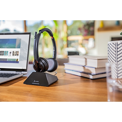 Black headset on stand, laptop and books on wooden surface. A room in the background.