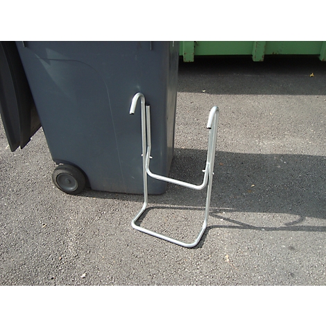 Poubelle grise avec un cadre métallique pour attacher des sacs poubelles sur de l'asphalte gris. Une poubelle verte est en arrière-plan.