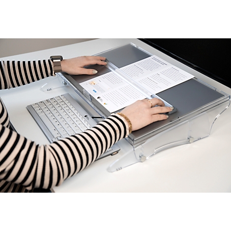 Une personne portant une bague, une montre-bracelet et un bracelet utilise un appareil de lecture spécial avec un clavier et une souris. Il y a du papier sur l'appareil de lecture.