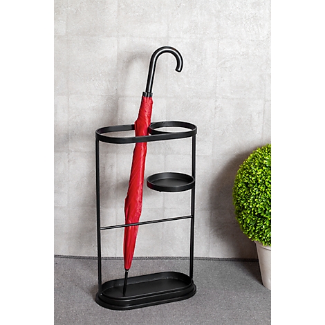 Porte-parapluie noir avec parapluie rouge, fond gris, plante verte à droite.