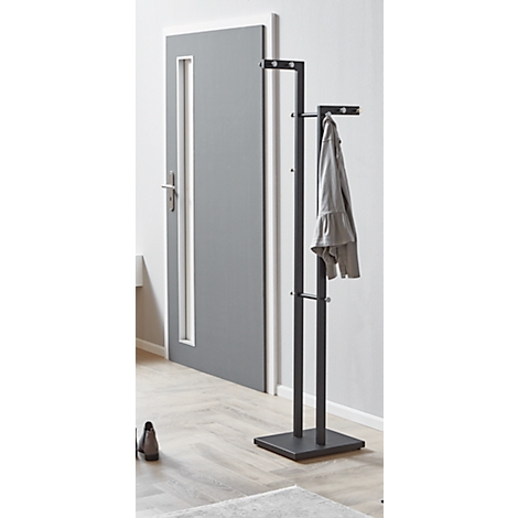 Portemanteau gris, autoportant, avec veste. Derrière le porte-manteau, une porte grise.