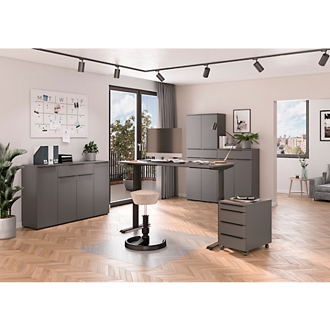 Een modern kantoor met een bureau, rolcontainer en kasten in grijs. Grote ramen en planten fleuren de kamer op.