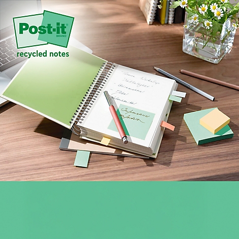 Notizbuch und Post-its auf Holzschreibtisch mit Stift und Blumen. Im Hintergrund Laptop. Post-it Logo.