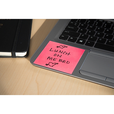 Ein pinkfarbener Notizzettel mit der Aufschrift „Lunch on me bro“ klebt auf einem Laptop, daneben ein schwarzes Notizbuch.