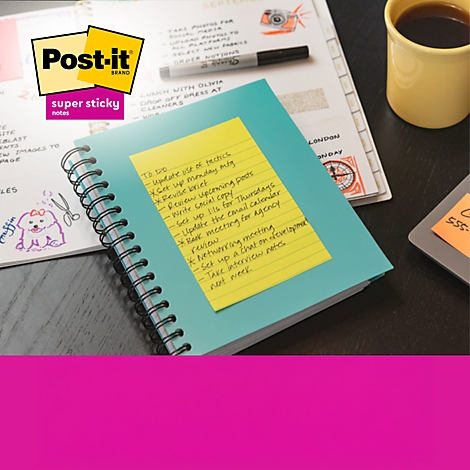 Een persoon schrijft aantekeningen op een gele Post-it die op een laptop is geplakt. Er zijn verschillende notitieboekjes en plaknotities in de scène.