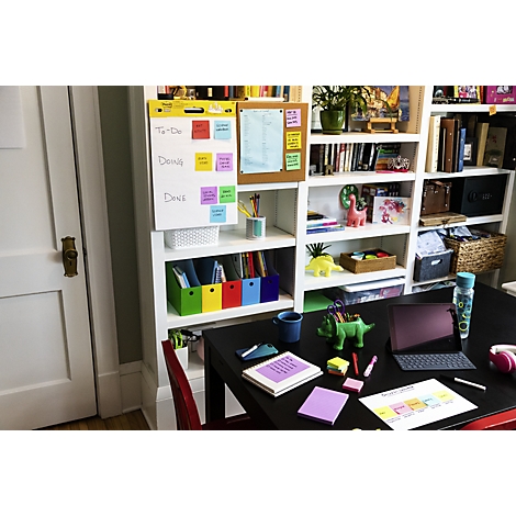 Desk with notes, laptop, and a green dinosaur pen holder. Bookshelf in the background.