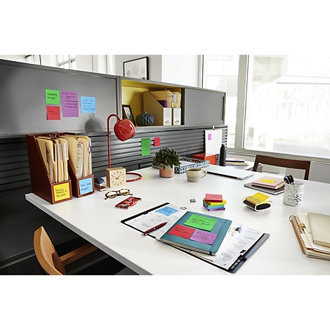 A desk with colorful sticky notes, folders, a lamp, and other office supplies. Focus on the sticky notes.