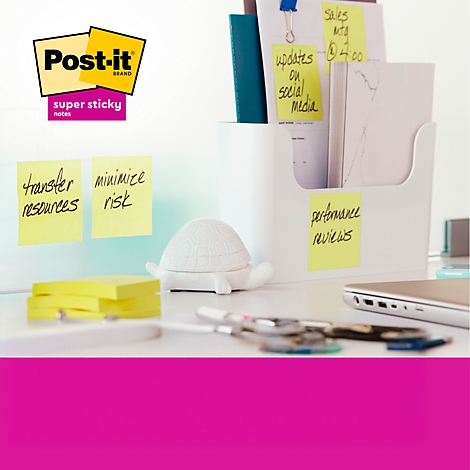 Close-up van een bureau met Post-it notes, pennen, een schildpadsculptuur en een laptop. Handgeschreven notities staan op de plaknotities.