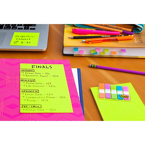 Nahaufnahme eines Schreibtischs mit Notizen, Stiften und einem Laptop. Gelbe Haftnotizen mit handschriftlichen Notizen. Ein Zettel trägt das Wort "FINALS".