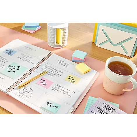 Un agenda avec des post-it, un stylo et une tasse de thé sur un bureau rose.