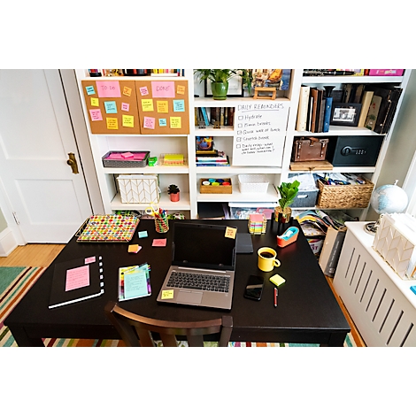 Bureau met laptop, notities, koffie, boeken en post-its. Op de achtergrond een plank met notities en boeken.
