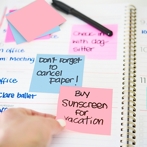 Close-up van een planner met post-its. Roze post-it leest: 'Koop zonnebrandcrème voor vakantie.'