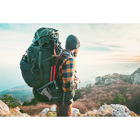 A hiker with a backpack stands on a mountain peak, looking into the distance.
