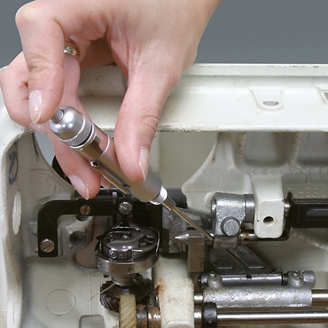 Eine Hand hält einen Schraubendreher und repariert eine Nähmaschine. Detailaufnahme, Nahaufnahme.