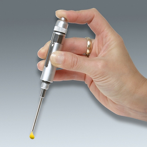 Hand hält eine Spritze. Am Ende der Nadel tropft eine gelbe Flüssigkeit.