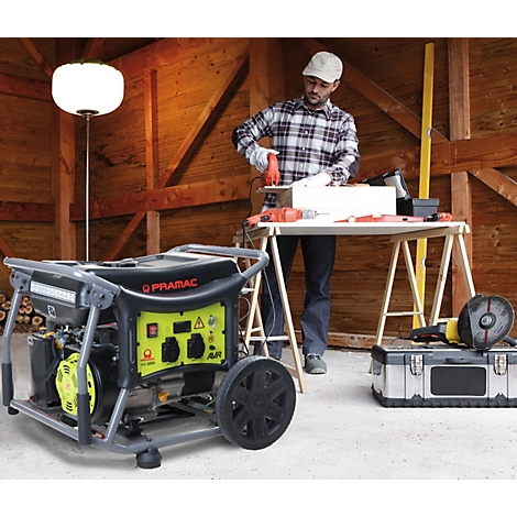 Ein Mann arbeitet in einer Holzwerkstatt mit elektrischen Werkzeugen, die von einem gelben Pramac-Stromerzeuger gespeist werden.