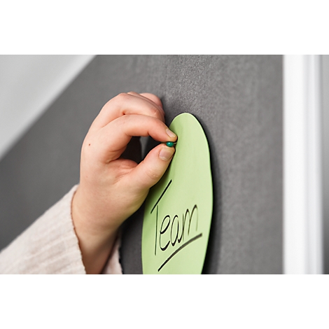 A hand presses a green pin onto a green leaf with the word Team on a dark bulletin board.