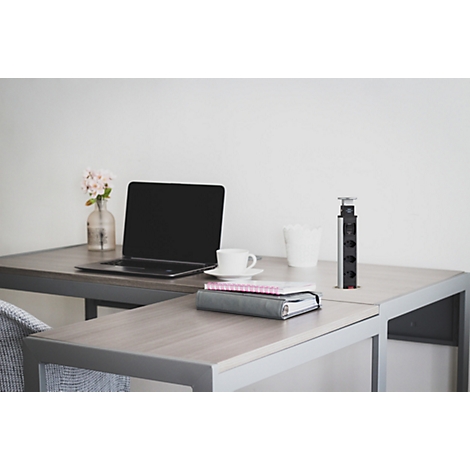 Un bureau moderne avec un ordinateur portable, une tasse de café, un vase de fleurs et une multiprise.