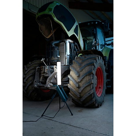 Un tracteur avec son capot ouvert, éclairé par une lampe de travail brillante et debout.