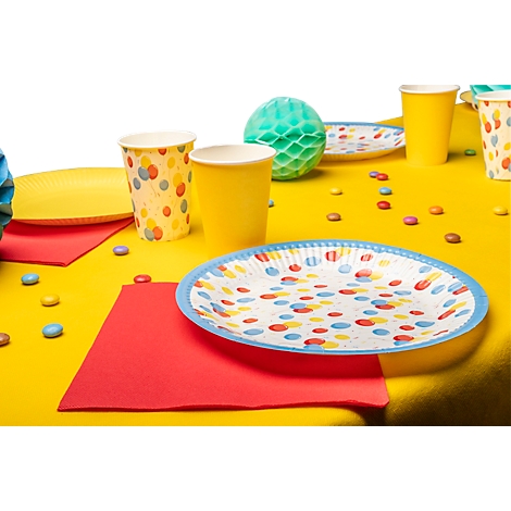 Table jaune avec décorations de fête : assiettes, gobelets, serviettes, bonbons et ballons.