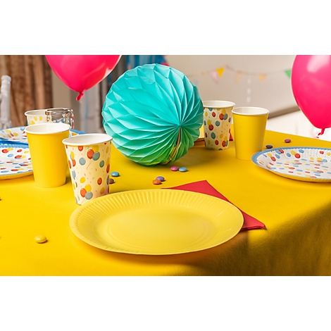 Ein festlich gedeckter Tisch mit gelber Tischdecke, gelben Papptellern und Bechern. Dazu Ballons, Dekorationen und Süssigkeiten.