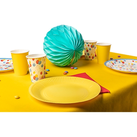 Gelber Tisch mit Partydeko: Teller, Becher, Luftballon. Bunte Süssigkeiten liegen verstreut.