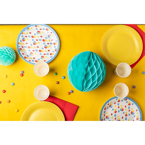 Gelber Tisch mit Party-Dekoration: Teller, Becher, Luftballons, Servietten und Süssigkeiten.