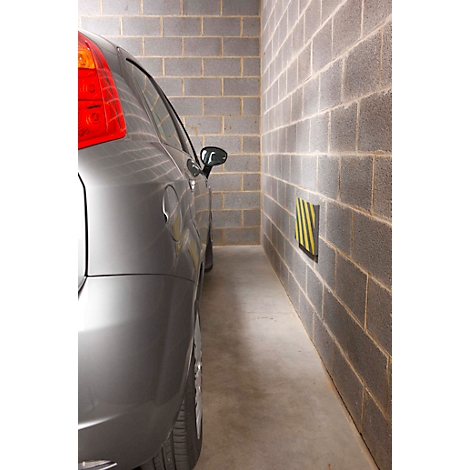 Voiture grise dans un garage étroit, mur avec protection jaune et noire.