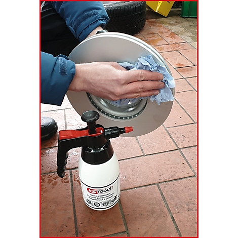 Eine Person reinigt eine Bremsscheibe mit einem blauen Tuch. Daneben steht ein Reiniger von KS TOOLS.