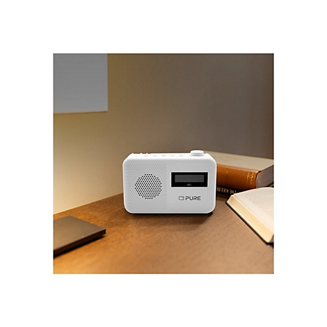 Weißes Radio mit rundem Lautsprecher und Display. Auf einem Holztisch, neben Büchern.