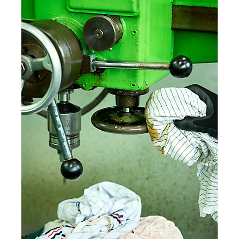 Detailaufnahme einer grünen Maschine mit Handrädern und Bedienhebeln. Ein Arbeiter putzt die Maschine.