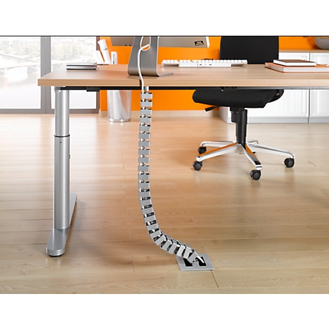 A metal cable duct on a height-adjustable desk. There is a monitor, keyboard and books on the table.