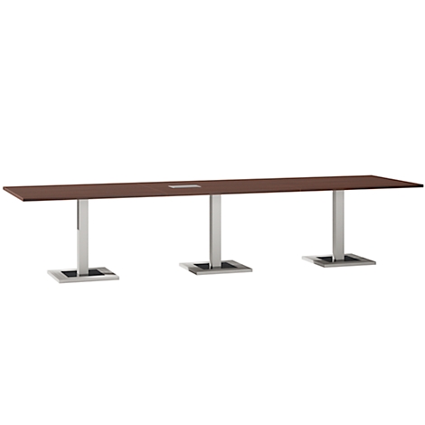 Long, rectangular conference table. The tabletop is brown, standing on three silver columns with square bases.