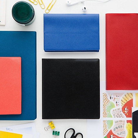 Vue aérienne de différents cahiers et fournitures de bureau sur fond blanc. Cahiers bleus, rouges et noirs disposés à côté d'accessoires.