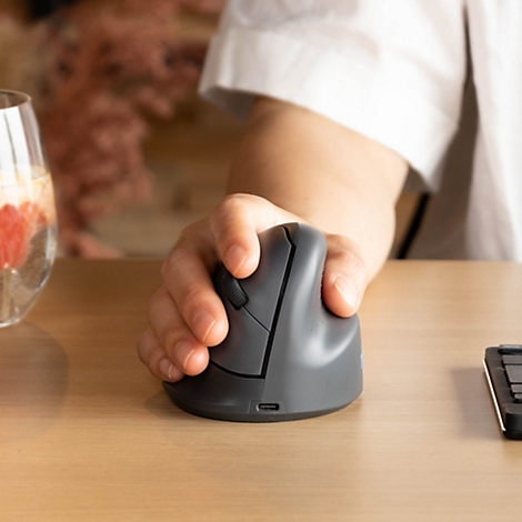 Eine Hand bedient eine ergonomische vertikale Computermaus auf einem hellen Holztisch.