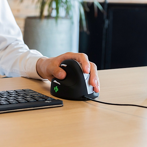 Eine Person benutzt eine vertikale Maus. Der Arm liegt auf dem Tisch, die Hand umfasst die ergonomische Maus.