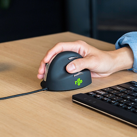Hand greift ergonomische Maus. Auf dem Tisch liegen zudem eine Tastatur und ein Kabel.