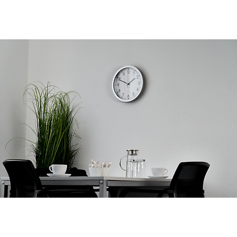 White clock on grey wall, table with teacups and decor.