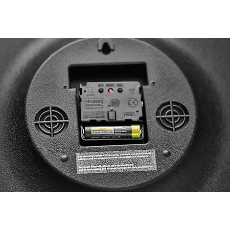 Close-up of the back of a clock with a battery installed. Black casing, ventilation slots, battery and clock mechanism visible.