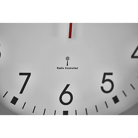 Close-up of a white radio clock, red hands, black numbers, radio symbol and lettering.