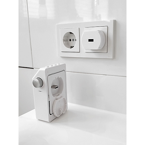 Une prise électrique blanche avec port USB. A côté, un chargeur blanc. Le tout sur un fond blanc.