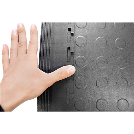 Helle Hand berührt schwarze, ineinandergreifende Bodenplatten mit Kreismuster und Verbindungsstücken.