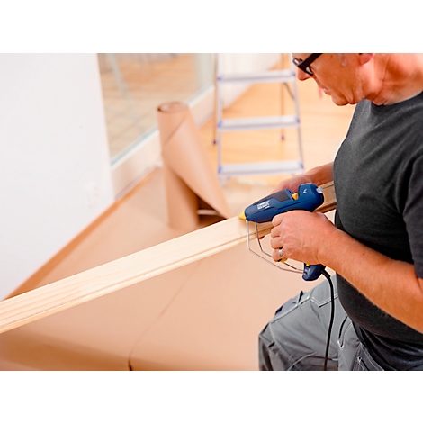 Man with glasses gluing a wooden strip. Ladder and paper roll in the background.