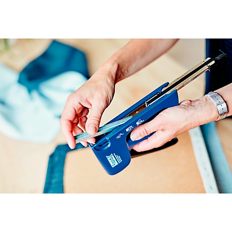 Person legt Heftklammern in einen blauen Tacker. Auf Tisch liegen blaue Stoffe.