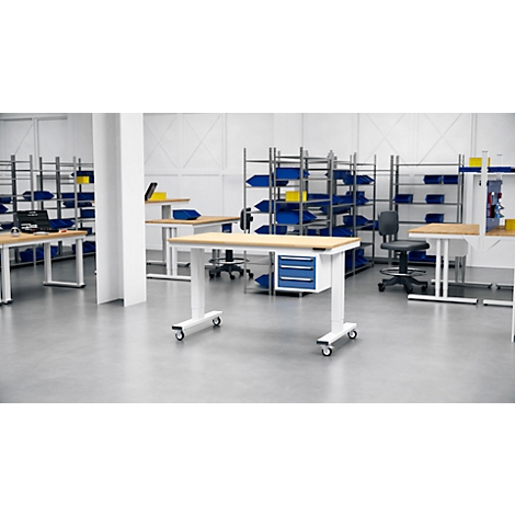 Ein Lagerraum mit Tischen, Regalen und Werkzeugkästen. Ein höhenverstellbarer Tisch steht im Mittelpunkt des Bildes.