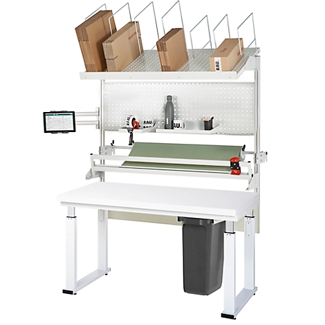 Weißer Packtisch mit Kartons, Grünpapier und Tablet. Schwarzer Mülleimer unter der Tischplatte.