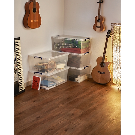 Three transparent storage boxes are in a corner of a room. Guitars and an accordion can be seen.