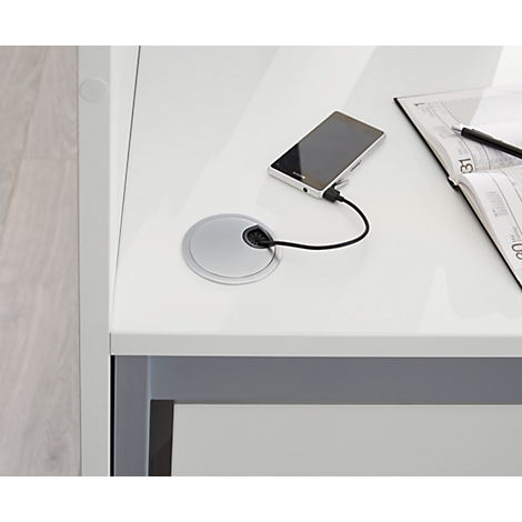 White desk with cable management. A smartphone is charging. A notebook and pen are lying next to it.
